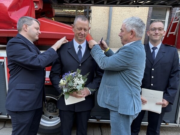 Paul Wehry (l.), Leiter des Brandschutzamtes, und Bürgermeister Thomas Beyer (2.v.r.) bringen Schulterstücke an der Uniform von Steffen Pittelkow an. Zuvor hatte Andreas Weber (r.) neue Schulterstücke erhalten. 