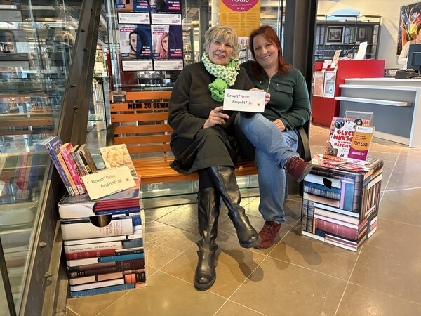 Petra Steffan (links), Gleichstellungsbeauftragte der Hansestadt Wismar, und Nastasja Henn von der Stadtbibliothek Wismar sitzen auf der orangefarbenen Bank.