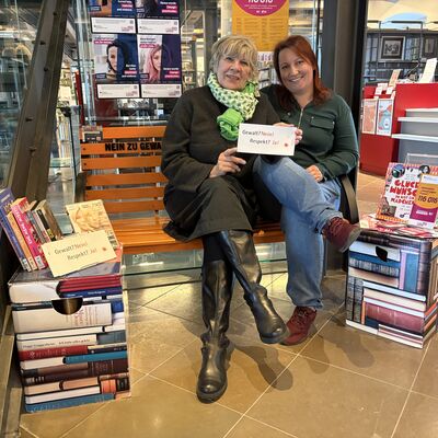 Petra Steffan (links), Gleichstellungsbeauftragte der Hansestadt Wismar, und Nastasja Henn von der Stadtbibliothek Wismar sitzen auf der orangefarbenen Bank.